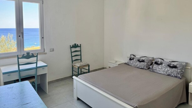Une chambre à coucher avec un lit, un bureau, une chaise et une fenêtre donnant sur la mer.