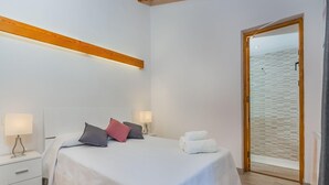 Et soveværelse med en seng, to sengeborde, et natbord, en træbjælke i loftet, en dør og udsigt til stranden.