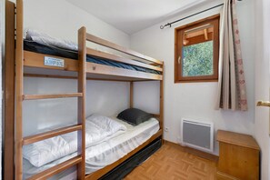 A bunk bed room with a window, a heater, and a wooden cabinet.
