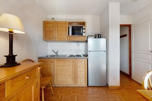 A compact kitchen with wooden cabinets, a microwave, a refrigerator, and a dining table with chairs. - Le 8D des Cimes La Toussuire (Villarembert)