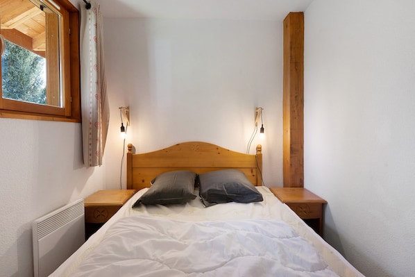 A bedroom with a wooden headboard, two bedside lamps, a radiator, and a window with curtains.