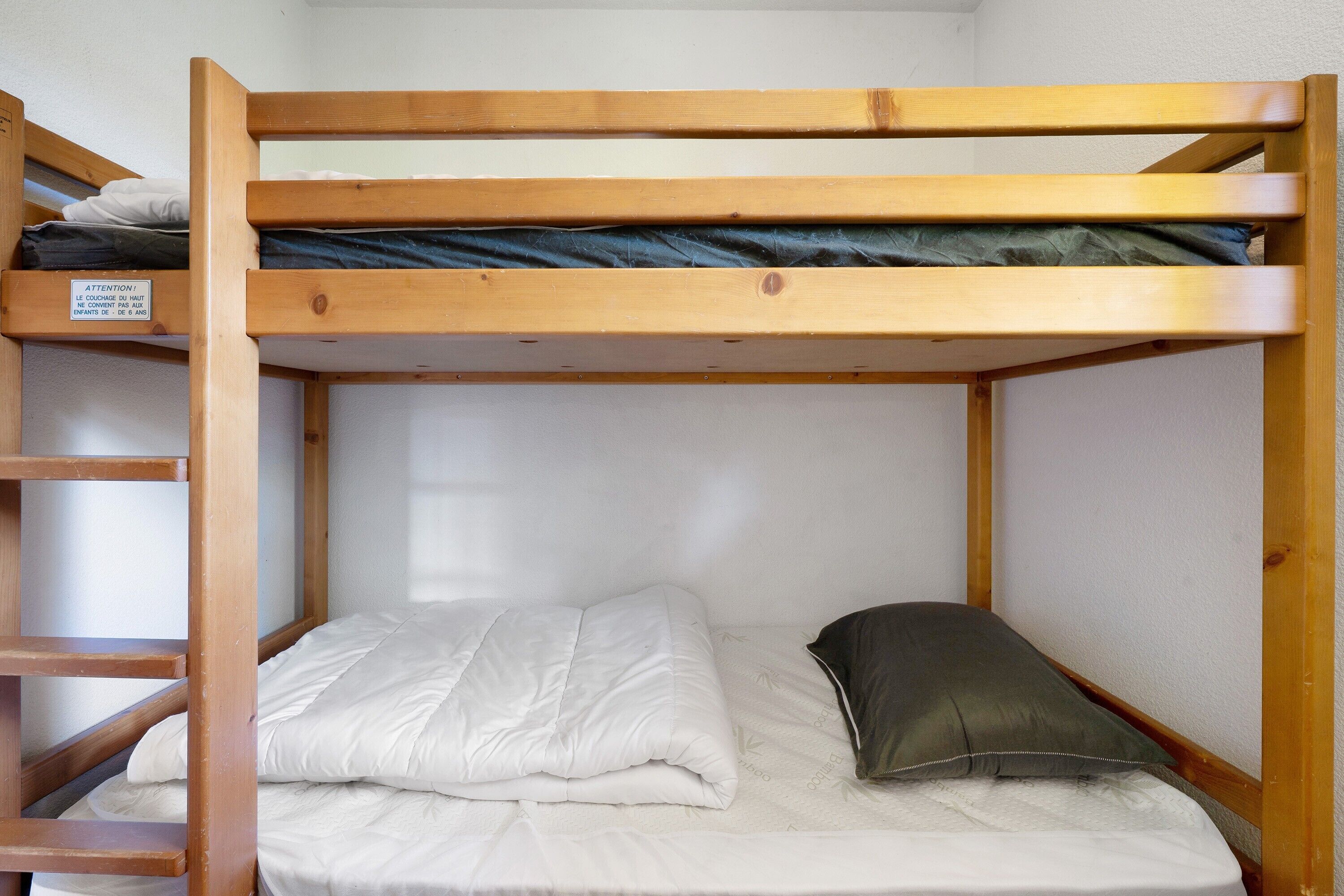 Un lit superposé avec un matelas et des oreillers, une échelle en bois et une étagère fixée au mur.