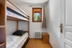 A small, compact room with a bunk bed, a radiator, a window with curtains, and a door.