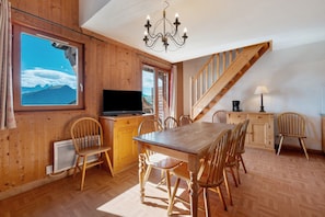A wooden interior with a dining table, chairs, a TV, and a view of mountains through a window.