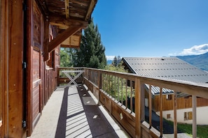 A wooden balcony with a view of mountains and a clear sky.