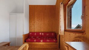 A wooden cabin interior with a sofa, a table, and a window with a view. - Le 8D des Cimes La Toussuire (Villarembert)