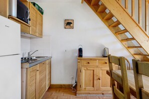 Ett kompakt kök med träskåp, en inbyggd mikrovågsugn och en liten matplats med en trästol.