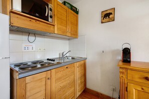 A kitchen with wooden cabinets, a stove, a microwave, and a kettle on a wooden countertop.