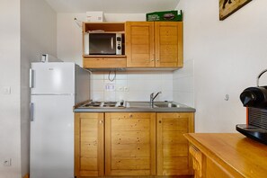 Eine kleine Küche mit Holzausstattung, einer Mikrowelle, einem Kühlschrank und einer Kaffeemaschine.
