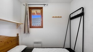 Un dormitori amb un llit, una finestra amb cortines, un radiador i un capçal de llit de fusta.