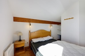 A bedroom with a wooden headboard, a bedside table with a lamp, and a bed with white bedding.