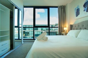 Ein Hotelzimmer mit einem großen Bett, einem Nachttisch, einem Fenster mit Blick auf Gebäude und einem Kleiderschrank.