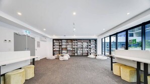 A modern library with white walls, a carpeted floor, and a large bookshelf. - Ultimate Comfort - Modern 3BR Apt with Pool and Gy (Adelaide)