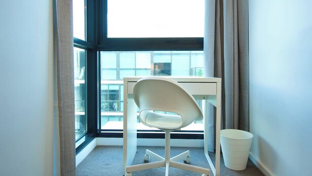 A corner room with a white desk, a chair, and a white trash bin. - Ultimate Comfort - Modern 3BR Apt with Pool and Gy (Adelaide)
