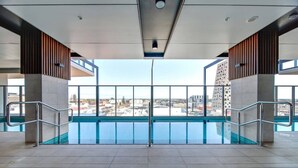 An indoor swimming pool with a view of the cityscape. - Ultimate Comfort - Modern 3BR Apt with Pool and Gy (Adelaide)