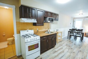Una cocina con estufa a gas, microondas, gabinetes oscuros y un comedor con sillas.