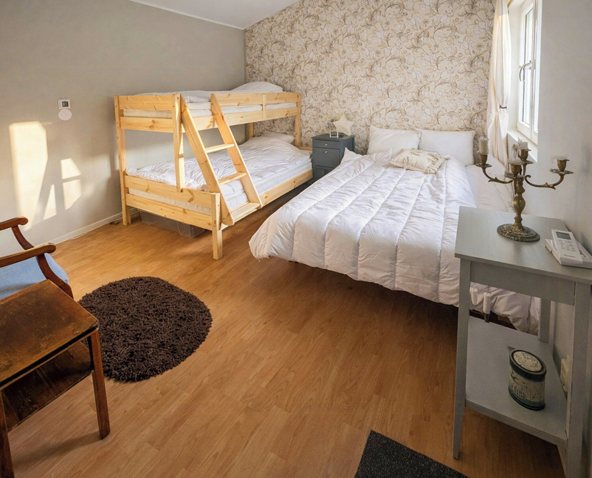 A bedroom with a bunk bed, a single bed, a desk with a lamp, and a chair.