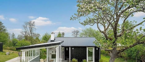 Una casa moderna con un cerramiento de vidrio, una terraza y un gran árbol en el jardín.