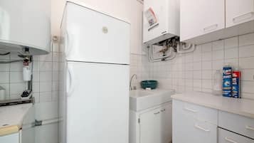 Una cocina con armarios blancos, un refrigerador blanco, un lavamanos con lavabo verde y un calentador de agua.