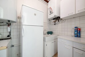 Et køkken med hvide skabe, et hvidt køleskab, en vask med en grøn kumme og en varmtvandsbeholder.