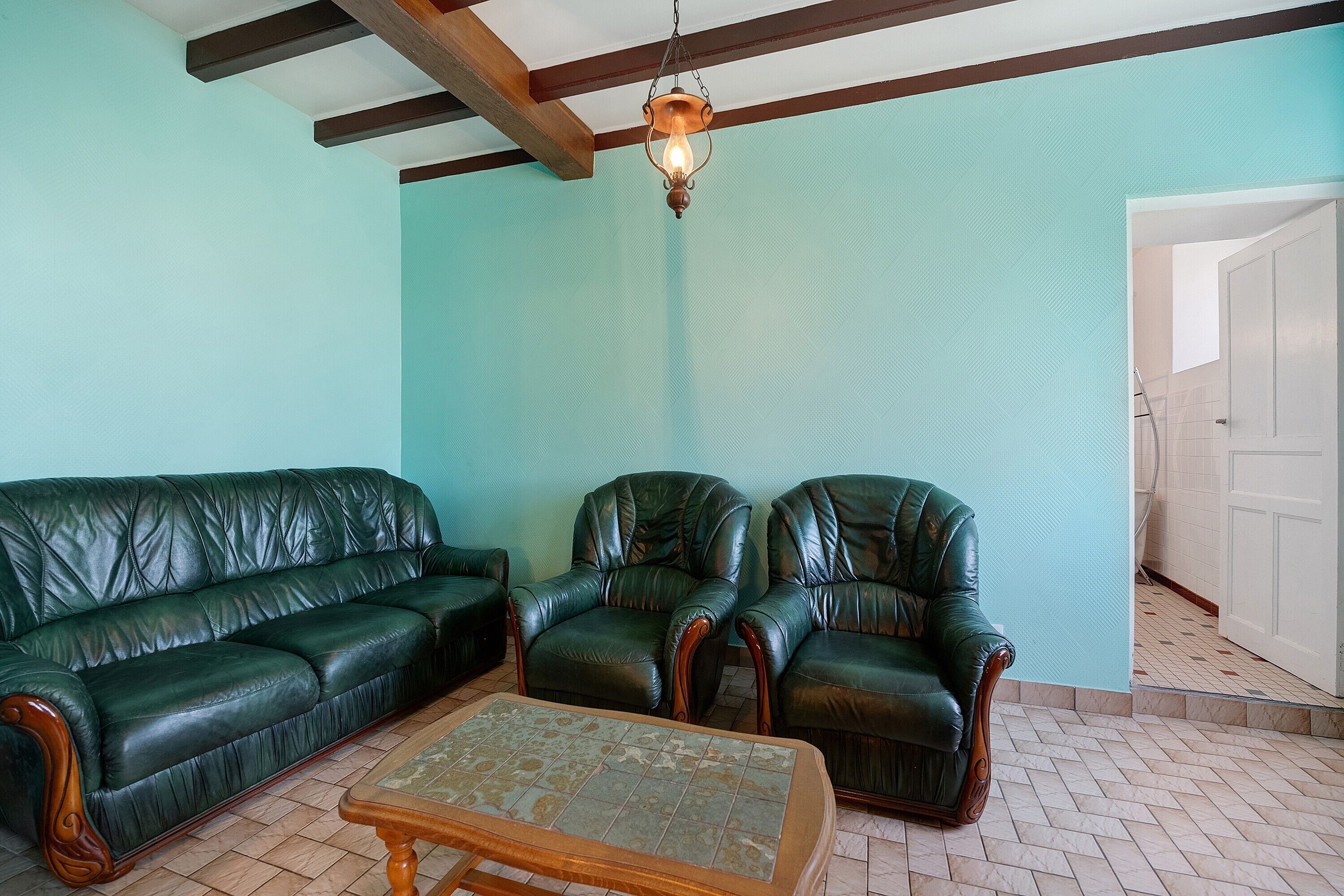 A room with a green leather sofa, two leather armchairs, and a wooden coffee table.