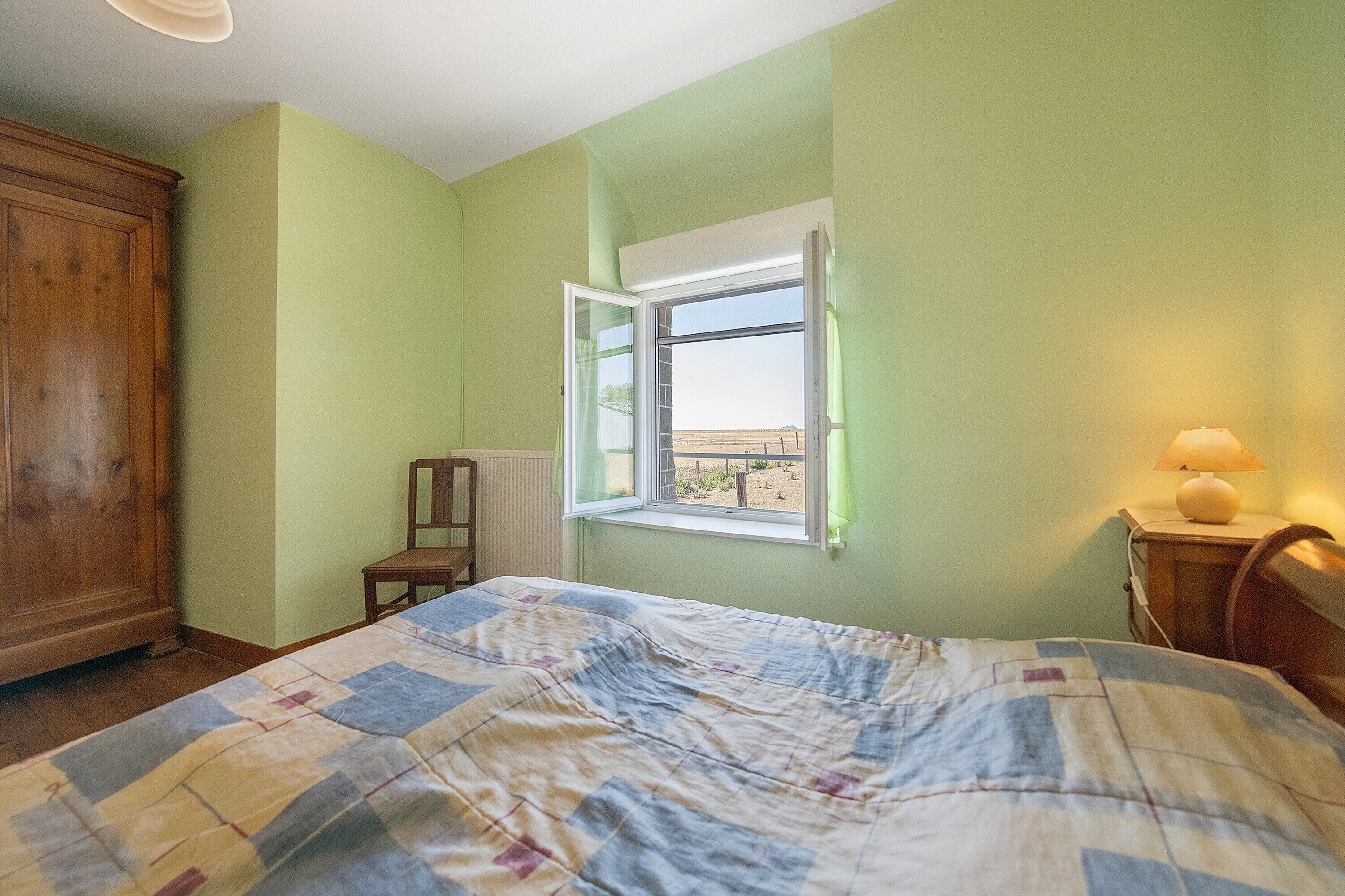 Un dormitorio con cama, armario de madera, ventana con vistas y lámpara de noche.