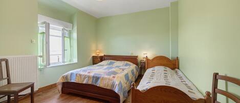 A bedroom with two wooden beds, a chair, a window with curtains, and a hanging light fixture.