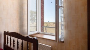 Een kamer met een raam dat uitkijkt op een landelijk landschap, een radiator en een houten stoel.