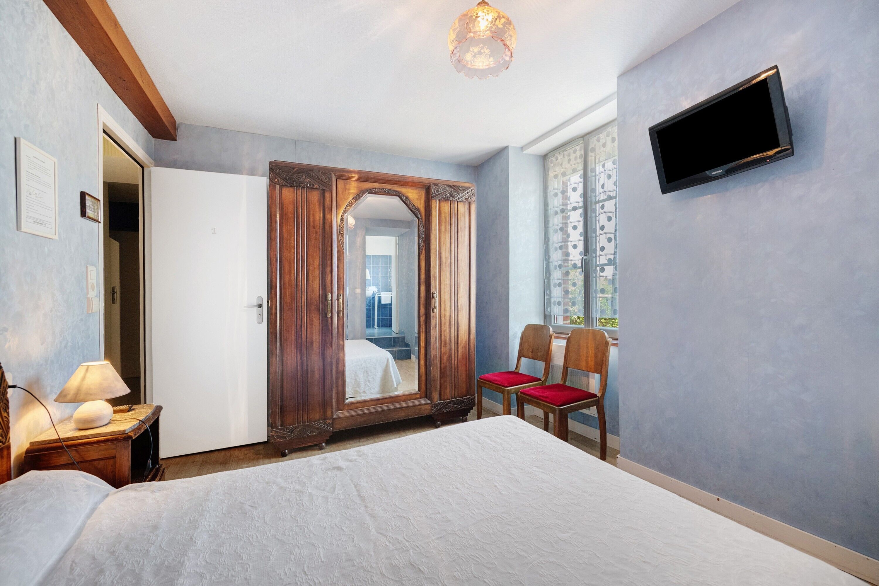 Habitación de hotel con una cama grande, un armario de madera, televisor montado en la pared y una ventana con vistas al exterior.