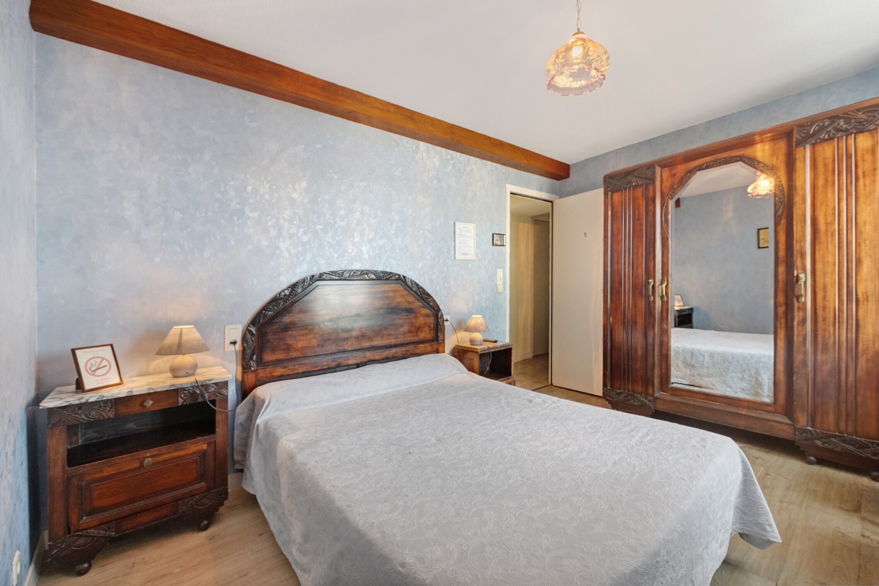 Un dormitorio con cama, mesita de noche, cómoda, espejo y puerta.