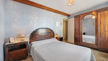 Un dormitorio con cama, mesita de noche, cómoda, espejo y puerta.