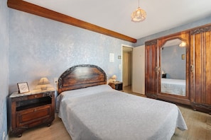 Une chambre à coucher avec un lit, une table de chevet, une commode, un miroir et une porte.