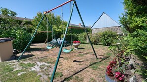 A backyard with a swing set, a garden with flowers, and a house in the background. - Guest Room "Chambre 1" with Wi-Fi (Courtils)
