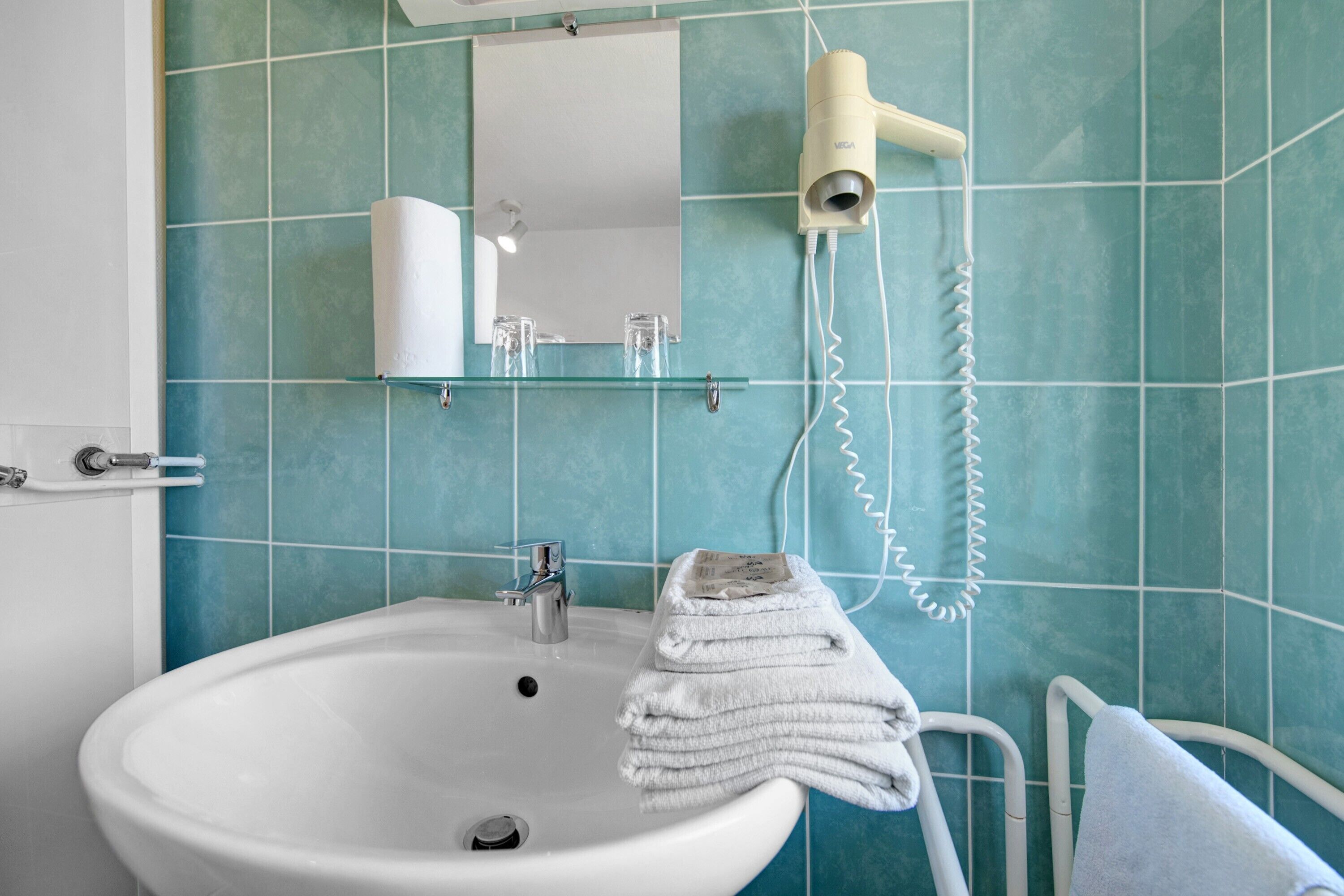 Een badkamer met een witte wastafel, een spiegel, een handdoekhouder en een haardroger aan de muur.