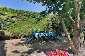 En have med et bord og stole, omgivet af grøn vegetation og et træ.