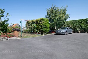 En boligkørsel med en parkeret bil, et gyngestativ og en have med plantekasser.