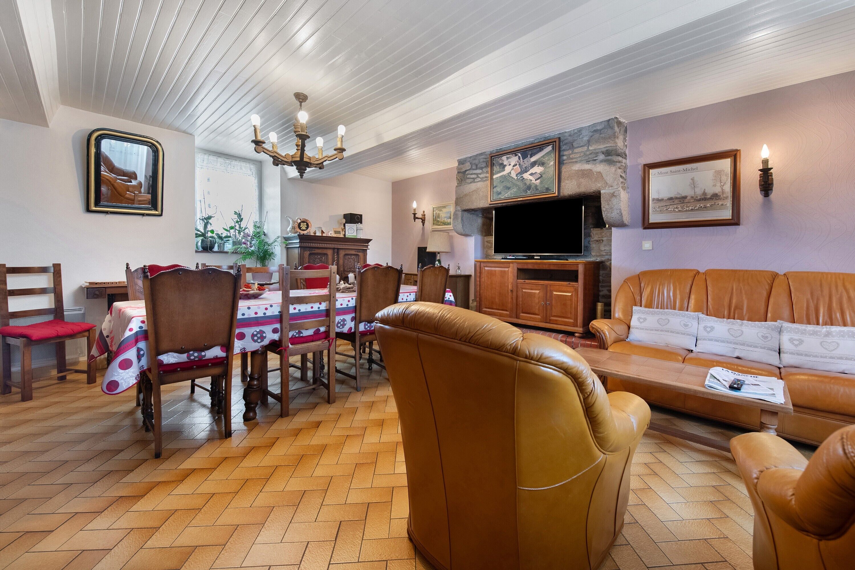 A living room with a sofa, chairs, a dining table with chairs, a television, and a fireplace.