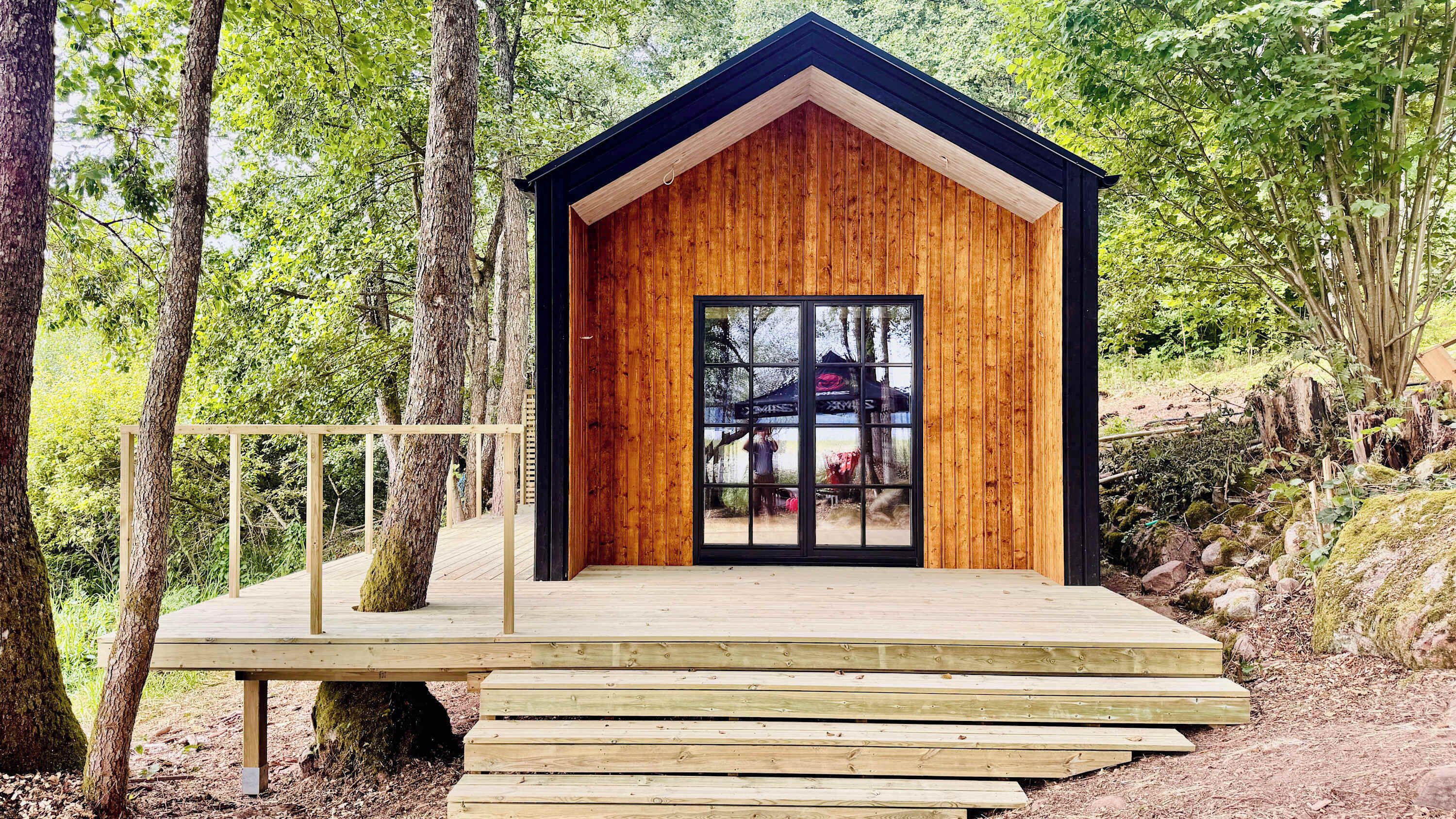A wooden cabin with a glass door, surrounded by trees.