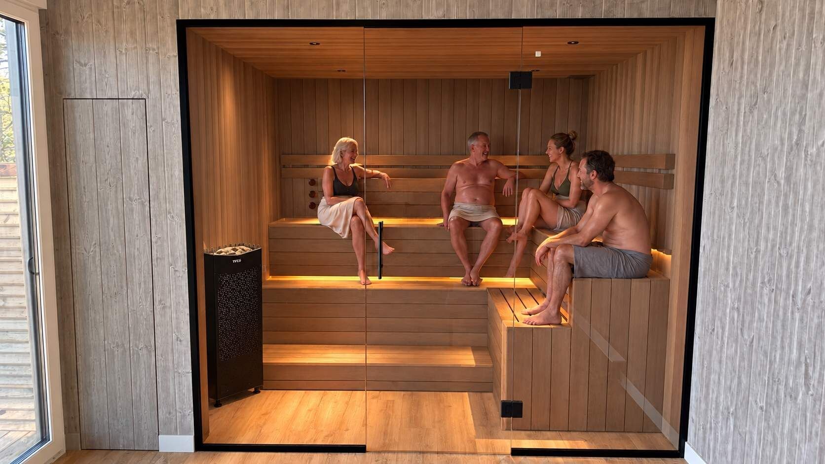 A sauna with wooden benches and a glass door, featuring a person performing a stretching exercise.