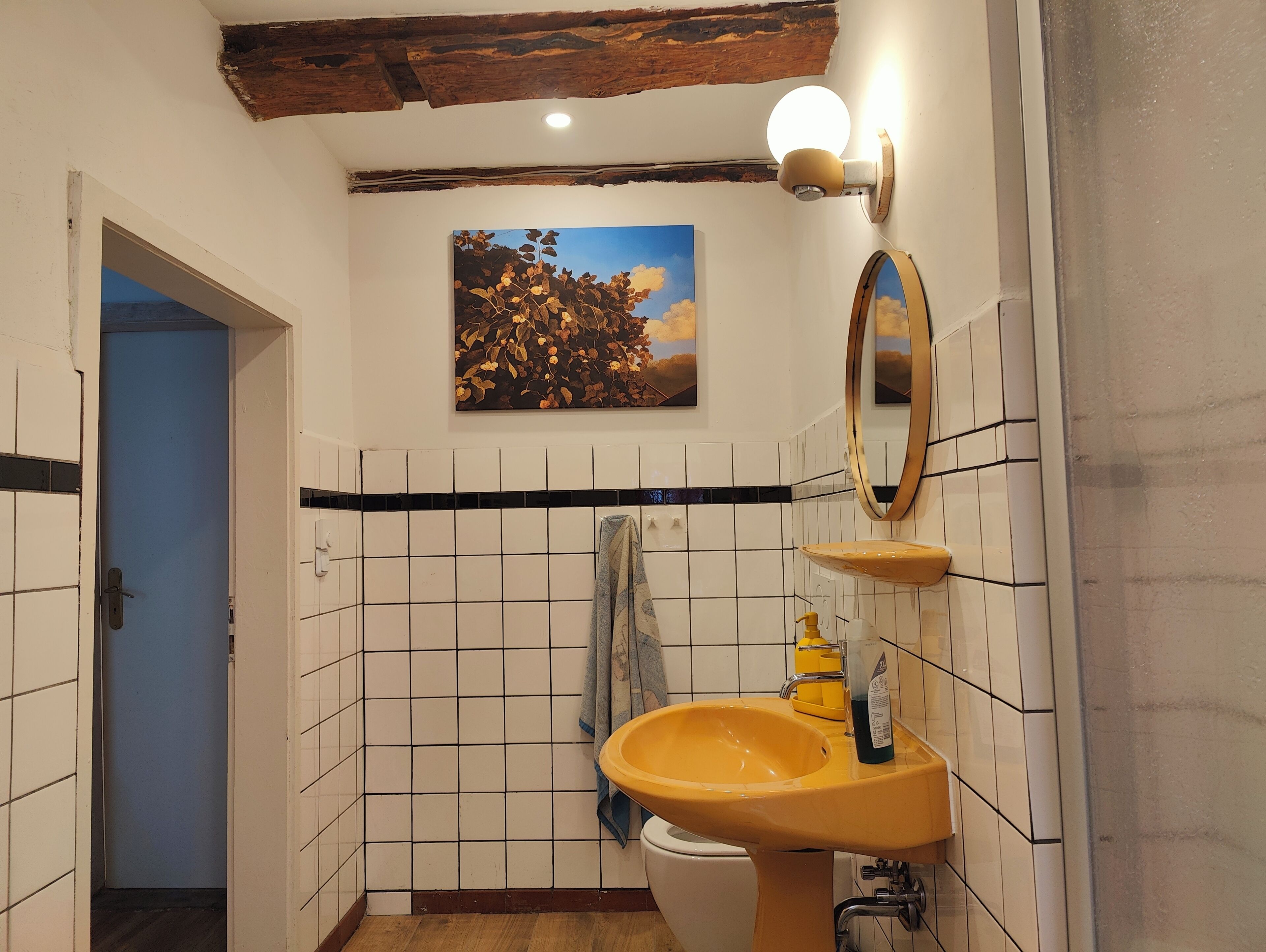 Een badkamer met een geel wastafel, een spiegel en een schilderij aan de muur.
