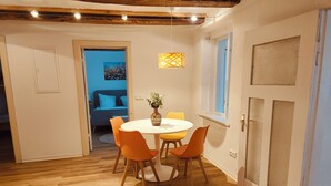 Un comedor con una mesa redonda, sillas color naranja y un florero con flores. Se observa una ventana con vistas al exterior.