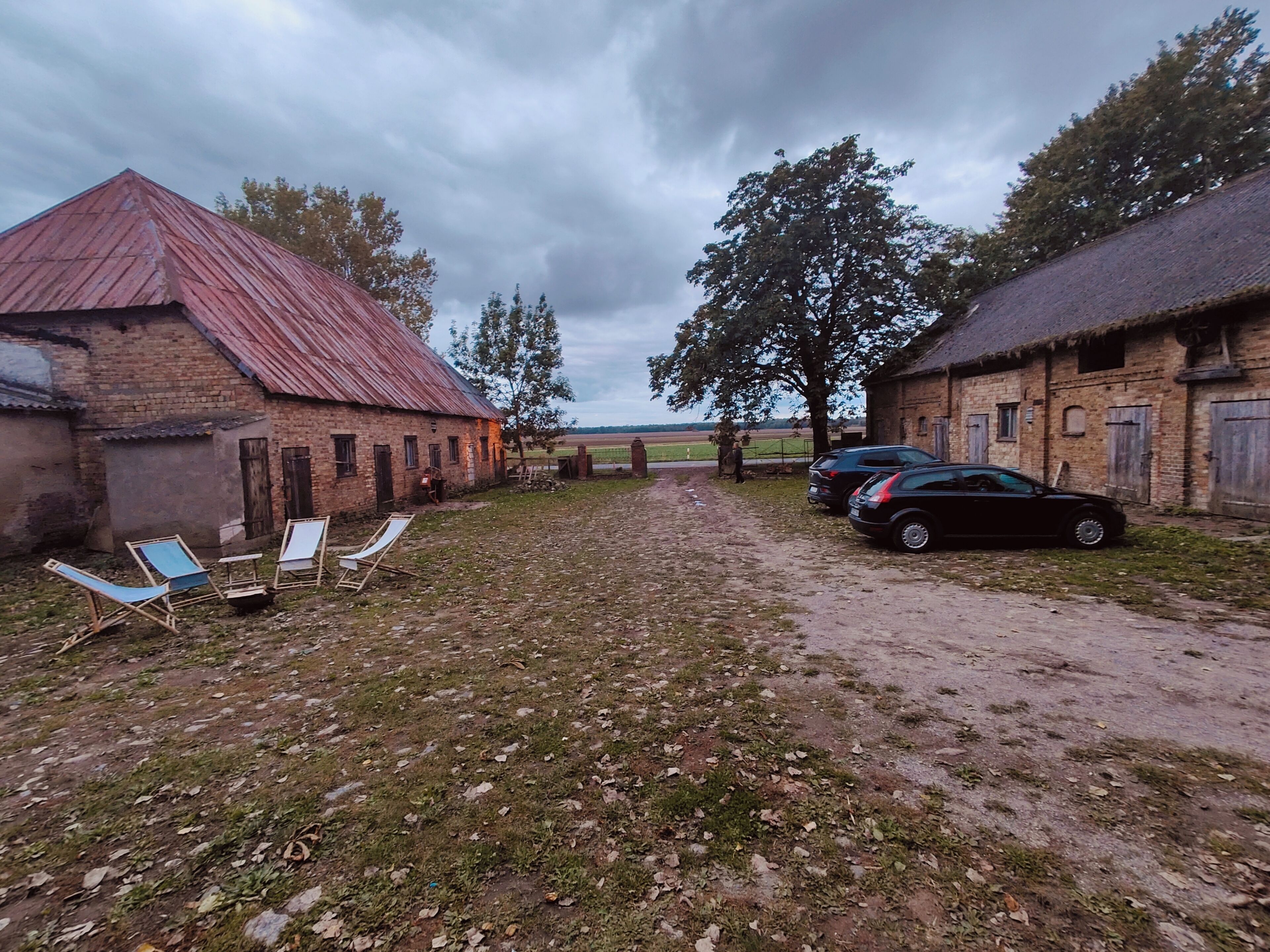 A rural setting with a dirt path, a barn, and a car parked on the side.