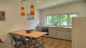 Una cocina moderna con una mesa de madera, sillas, un refrigerador y una ventana con vistas a la vegetación.