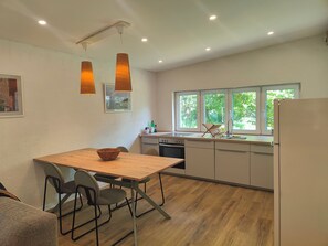 Una cocina moderna con una mesa de madera, sillas, un refrigerador y una ventana con vistas a la vegetación.