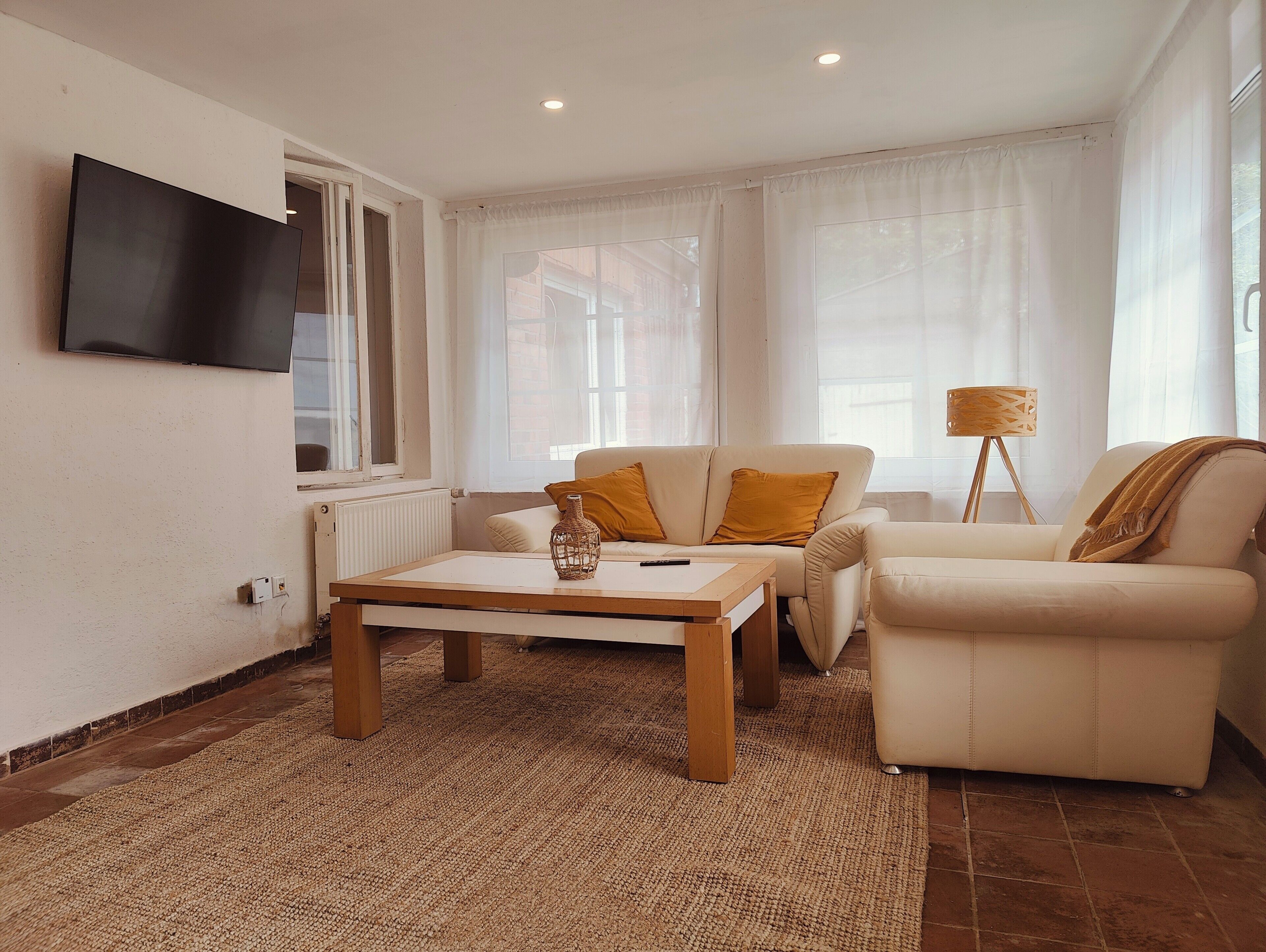 Un salon avec un téléviseur à écran plat fixé au mur, une table basse en bois, deux canapés et un lampadaire.