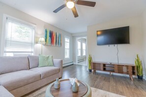 A living room with a sofa, a coffee table, a TV, and a ceiling fan.