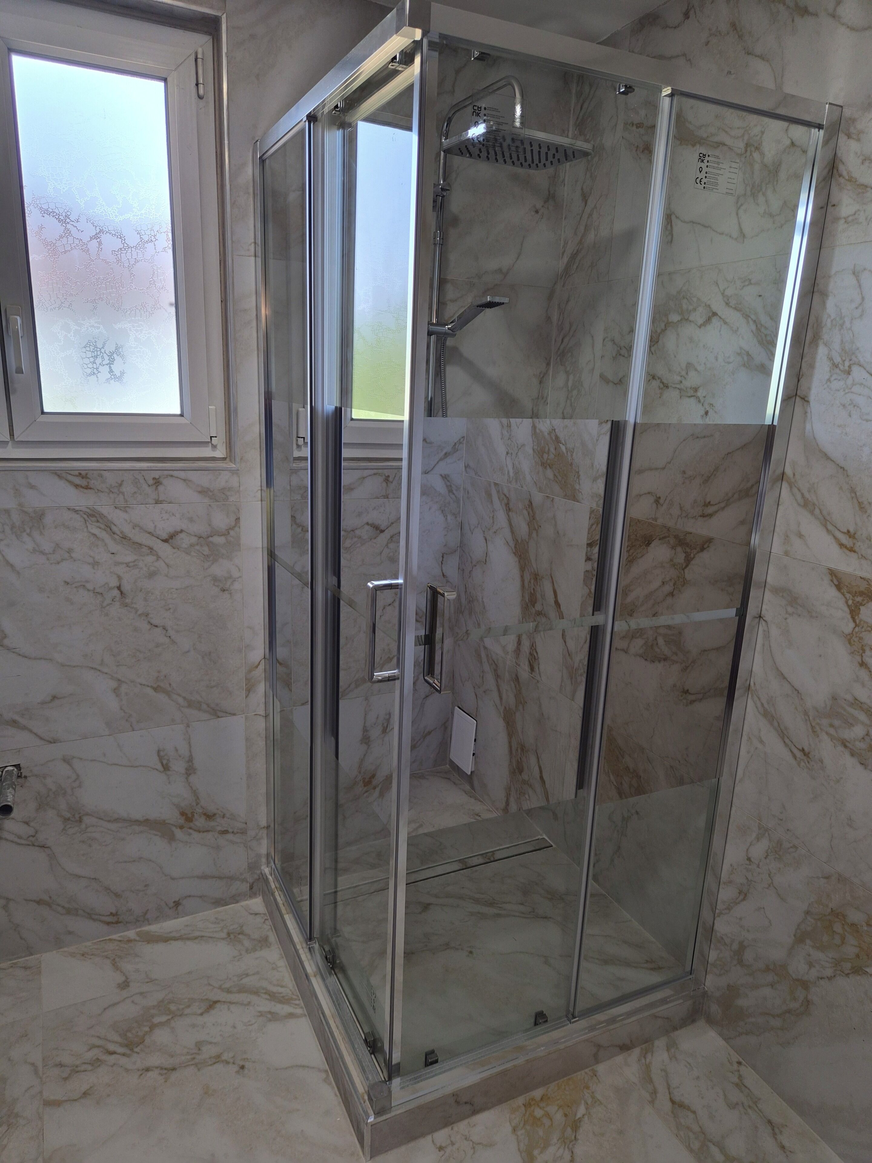 Une cabine de douche fermée par des parois en verre, dotée d’un pommeau de douche à main et d’un robinet fixé au mur.