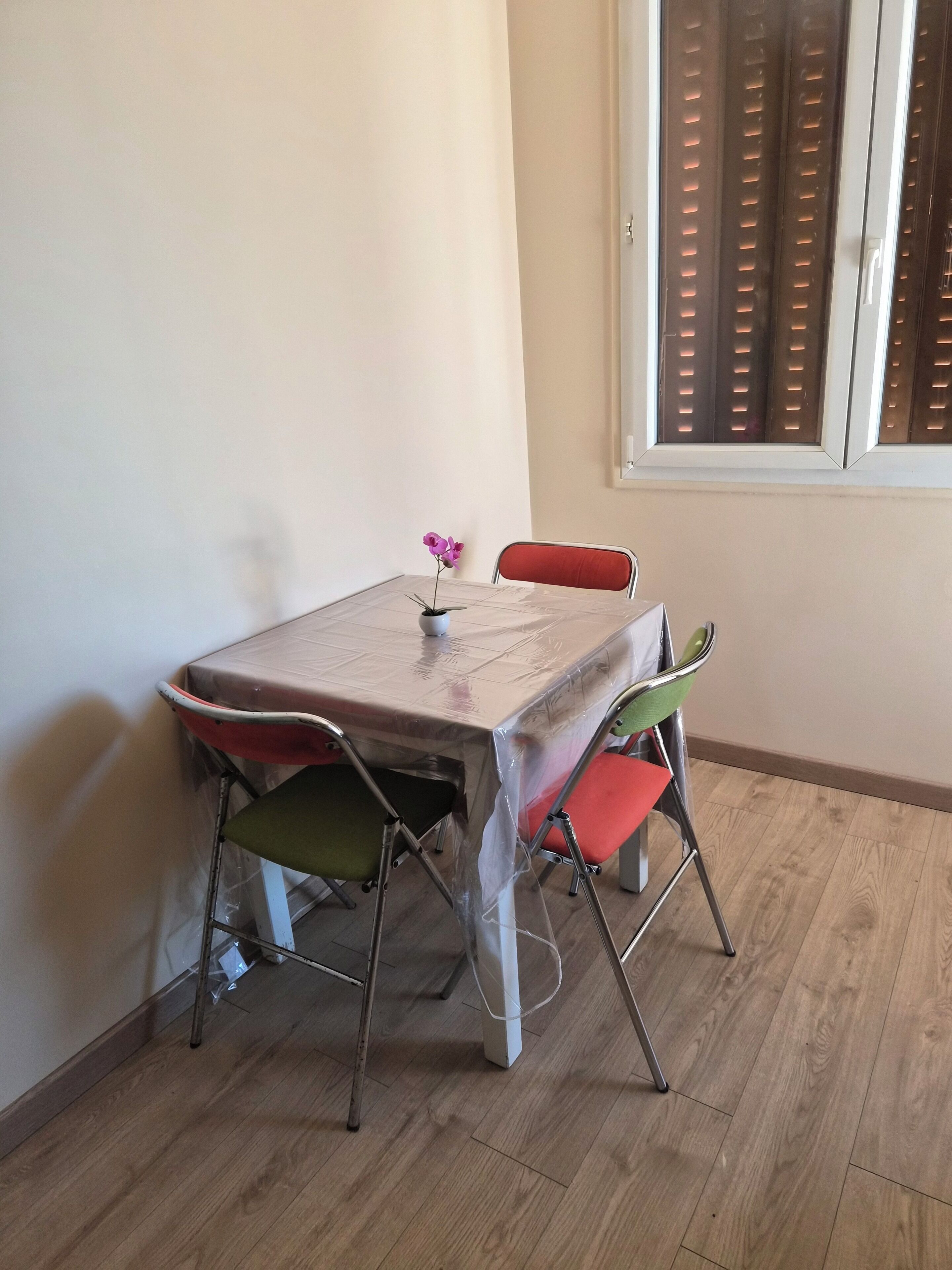 A small dining area with a table covered by a protective sheet, four chairs, and a potted plant.
