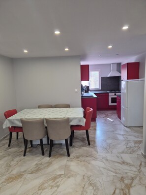 Un coin repas avec une table et des chaises, une cuisine avec des meubles rouges et un réfrigérateur blanc.