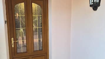 Eine Holztür mit Glasscheiben, eine an der Wand befestigte Leuchte und ein Fliesenboden.